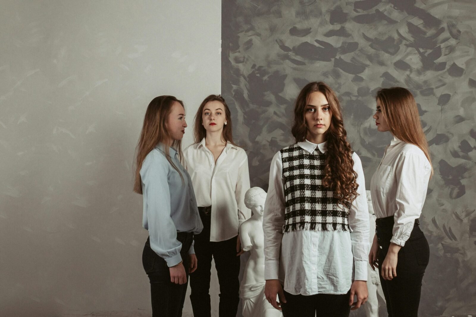 Stylish women in formalwear posing elegantly indoors with a classic sculpture backdrop.