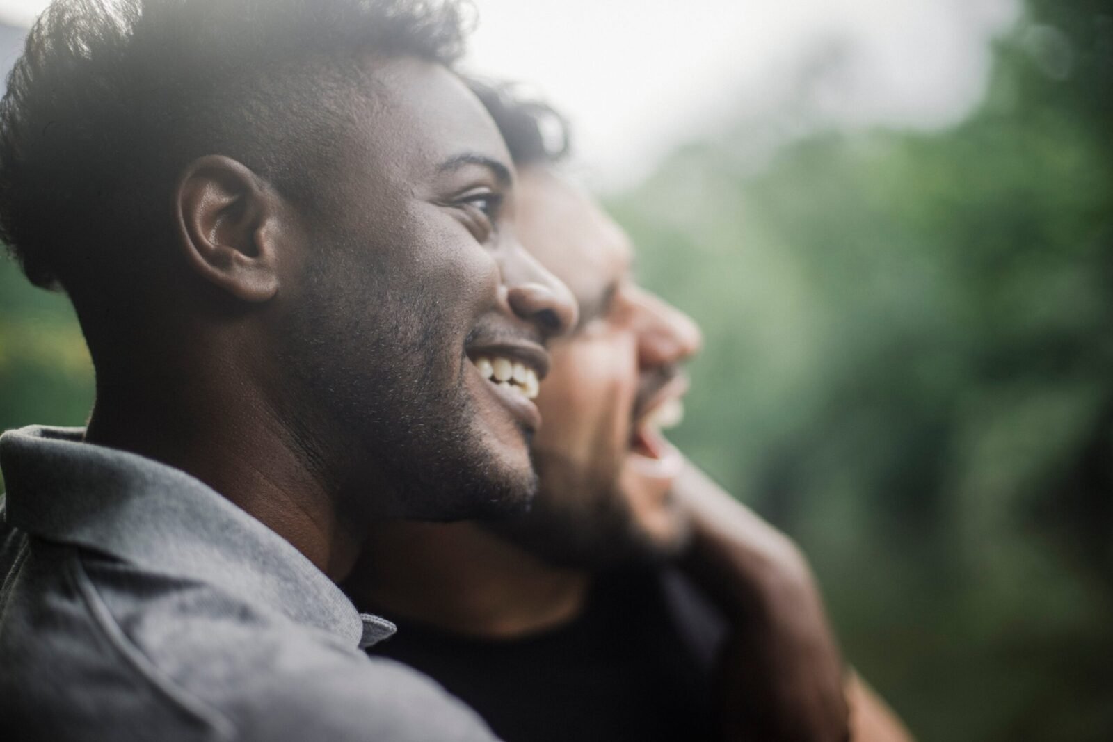 Close-up of two friends smiling happily outdoors. Bright, joyful connection captured in a lush natural setting.