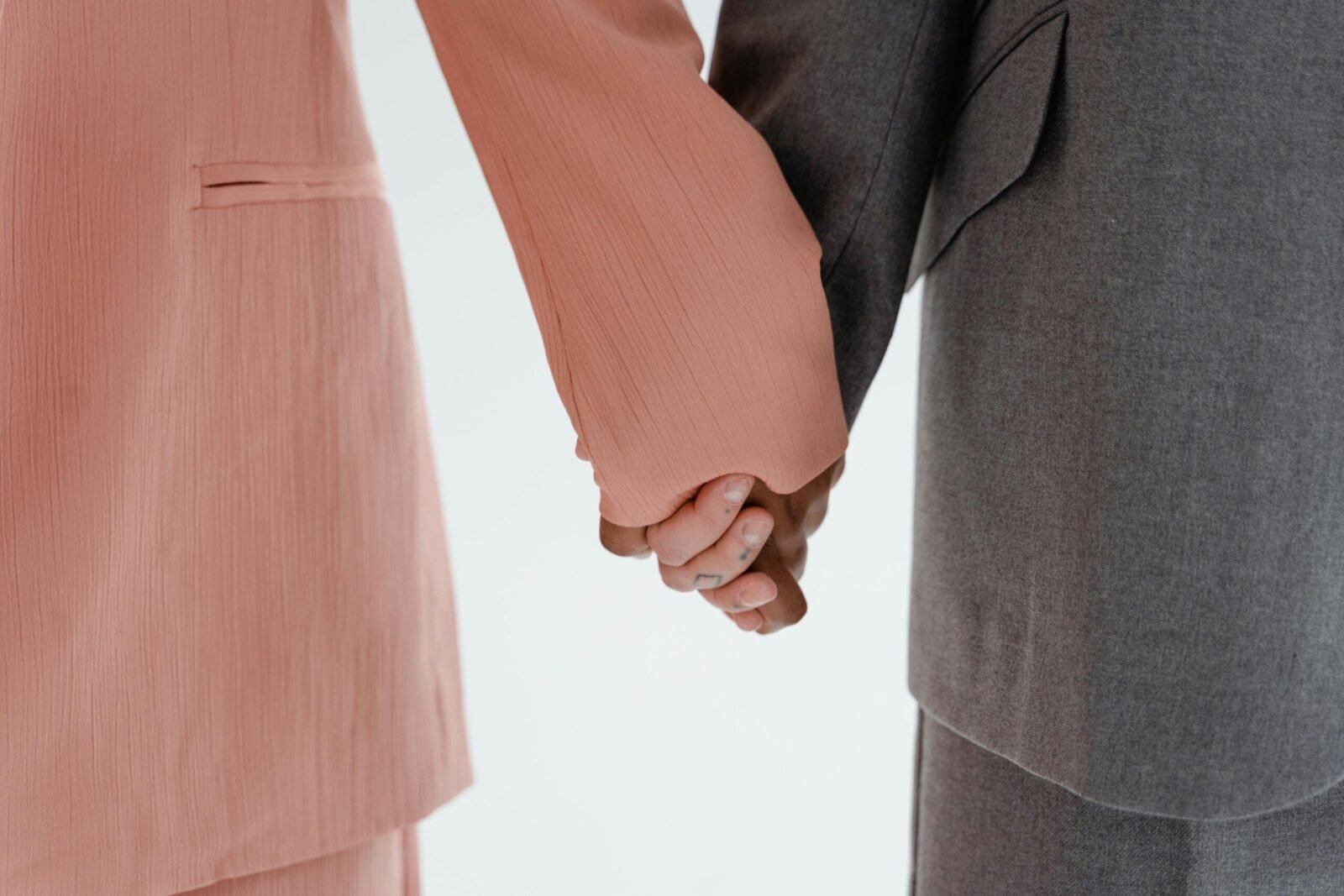 Close-up view of two people holding hands, wearing pink and grey suits, isolated on a white background.