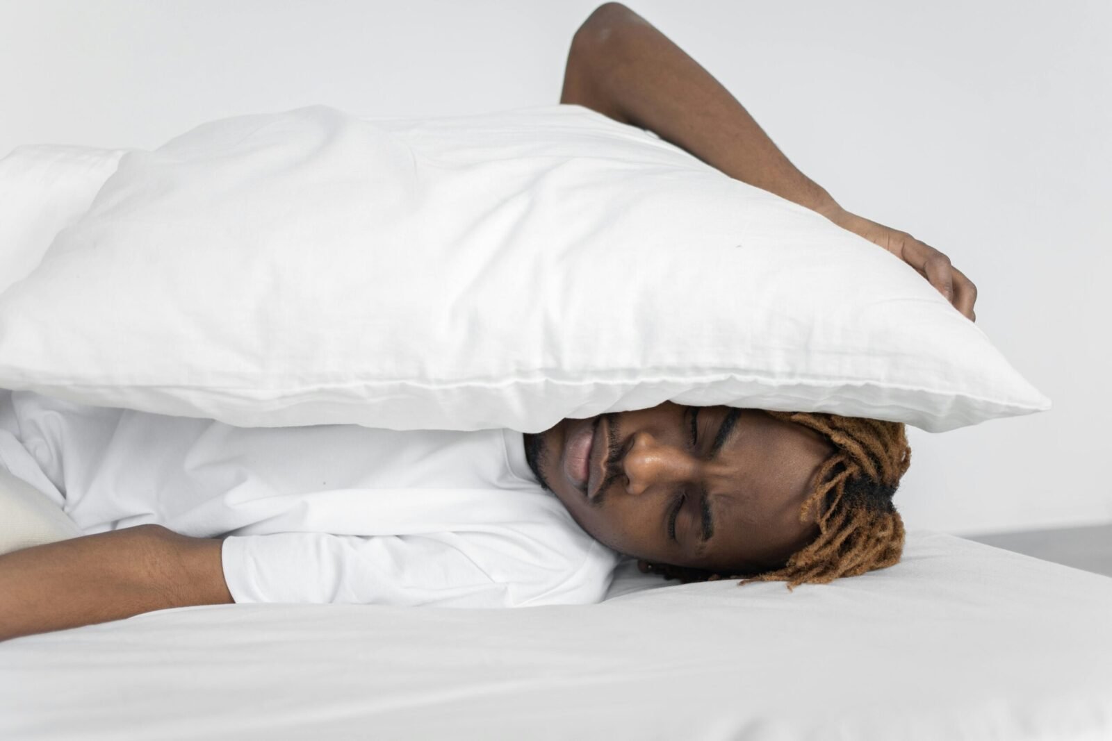 A man enjoying a peaceful nap indoors under a white pillow, conveying relaxation.