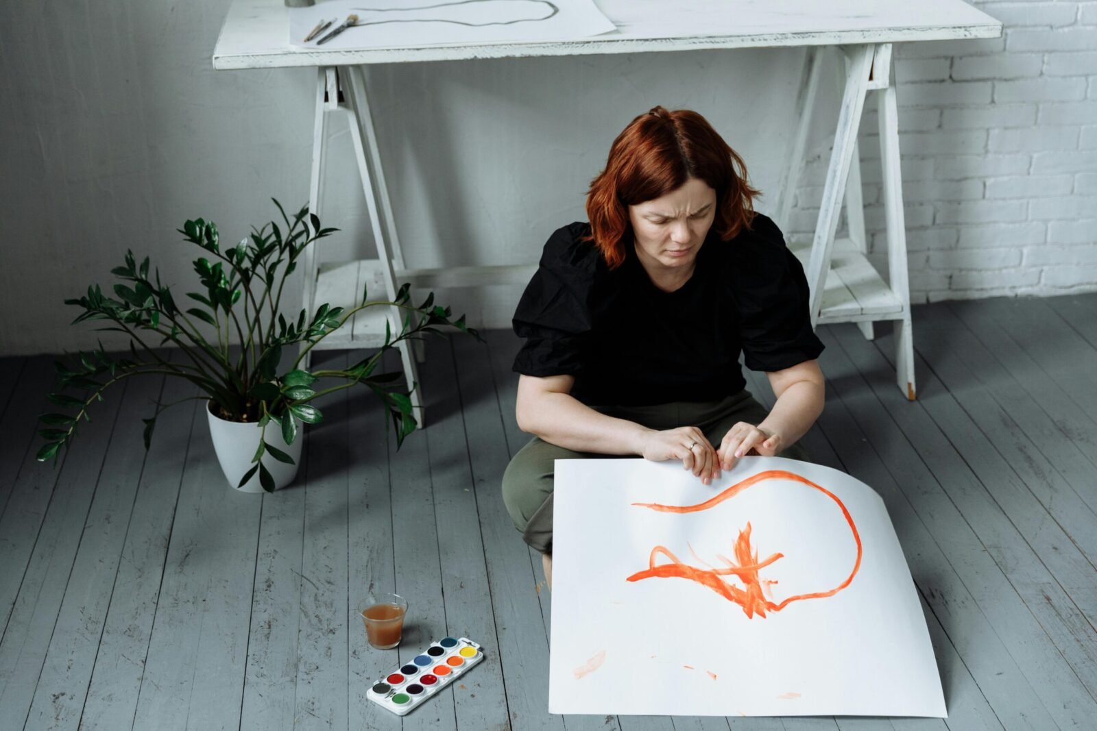 Caucasian woman sitting on studio floor, creating an abstract painting with watercolors.