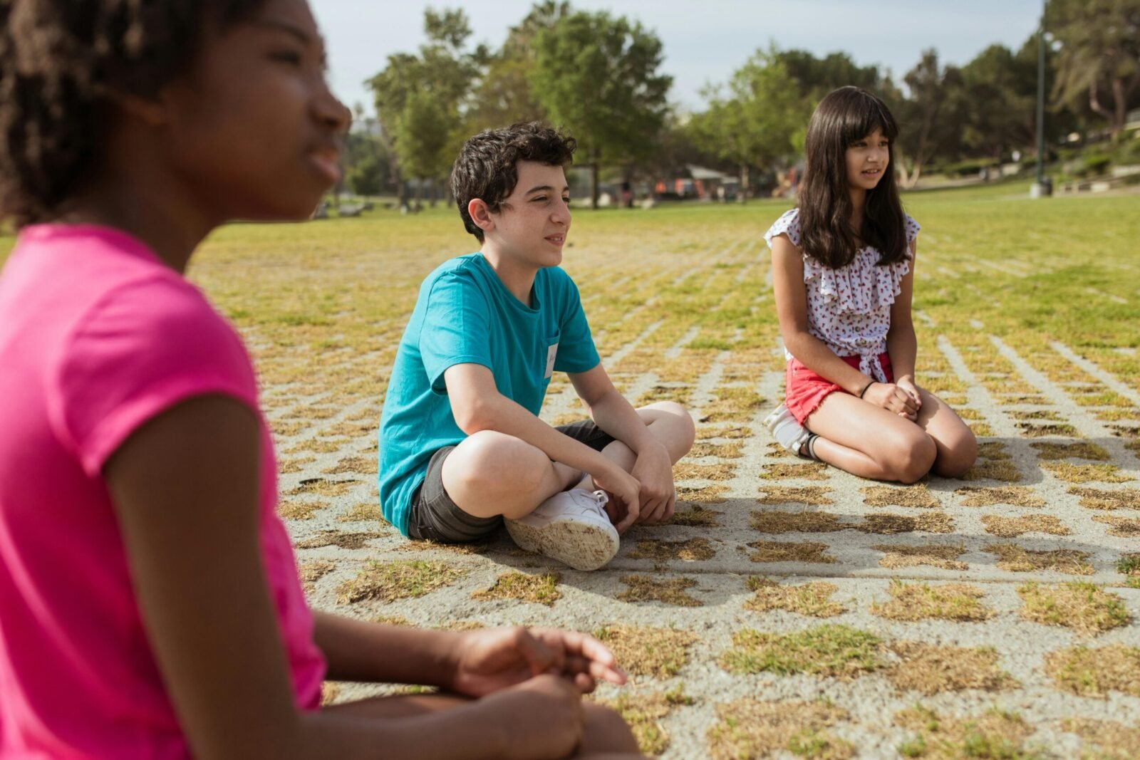 Kids sitting together in a green park during summer camp for team building and fun.